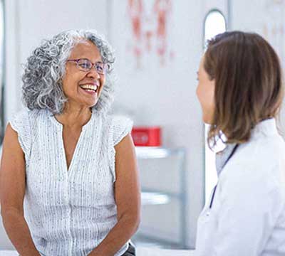 Photo-of-woman-smiling-and-talking-to-her-primary-care-provider-in-a-hospital-setting-news 